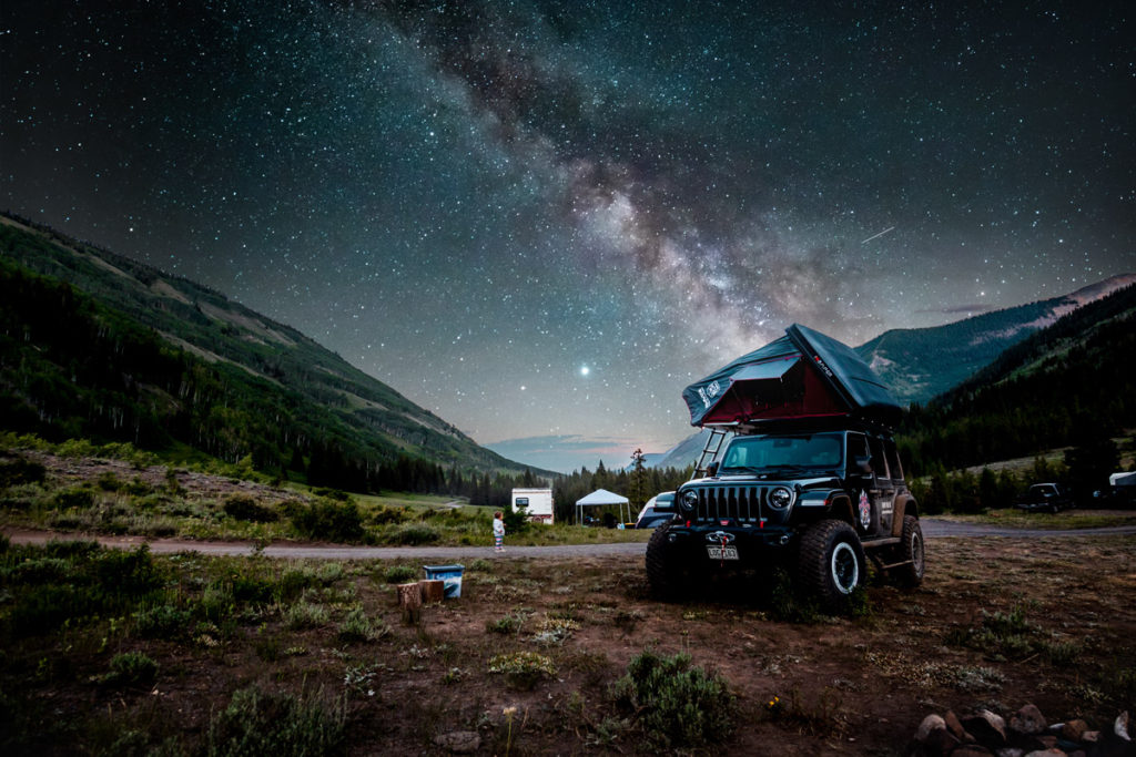 Jeep with a rooftop popup tent and the Milky Way in the background across the sky